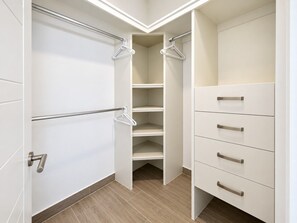 Um closet espaçoso com portas abertas, uma barra de metal para pendurar roupas e um conjunto de gavetas com puxadores.