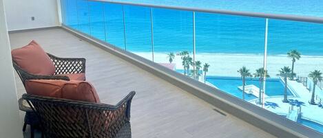 A balcony with wicker chairs, a pool, and a view of the ocean.