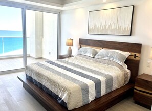 A modern bedroom with a large bed, a view of the sea, and a minimalist decor.