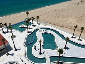 An aerial view of a resort with multiple swimming pools, palm trees, and a beach.
