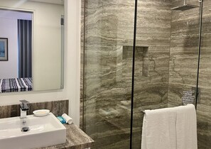 A bathroom with a marble shower enclosure, a sink with a mirror, and a towel rack.