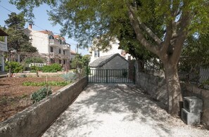 A residential area with a gated entrance, a tree-lined pathway, and a stone wall. - Apartment Villa DD (Supetar)
