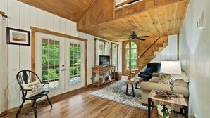 Ein geräumiges Wohnzimmer mit Holzböden und hohen Decken, ausgestattet mit einem Sofa, einem Fernseher und einer Treppe zu einer oberen Ebene.
