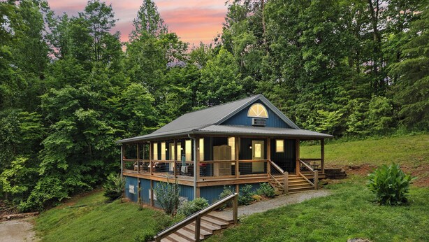Eine Lodge mit überdachter Terrasse, einer Treppe und Blick auf den umliegenden Wald.