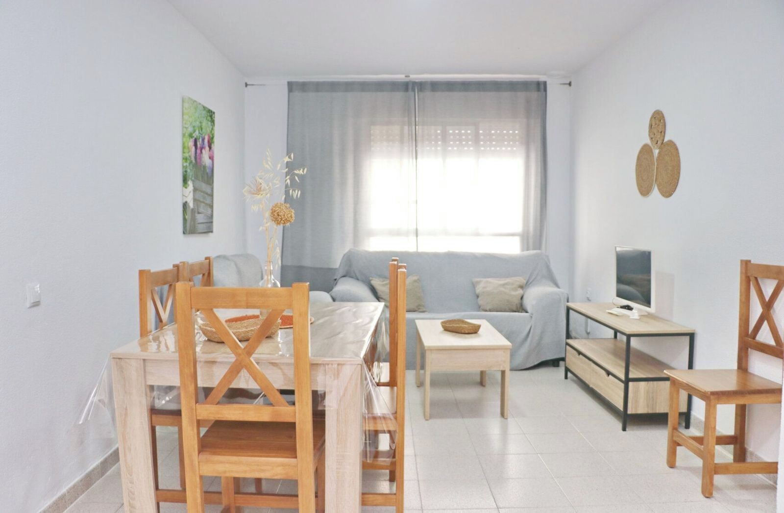 Una sala de estar moderna con comedor, un sofá, un televisor y una ventana con cortinas.