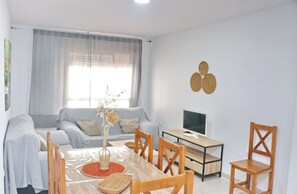 A living room with a sofa, TV, dining table, chairs, and a vase with dried plants.