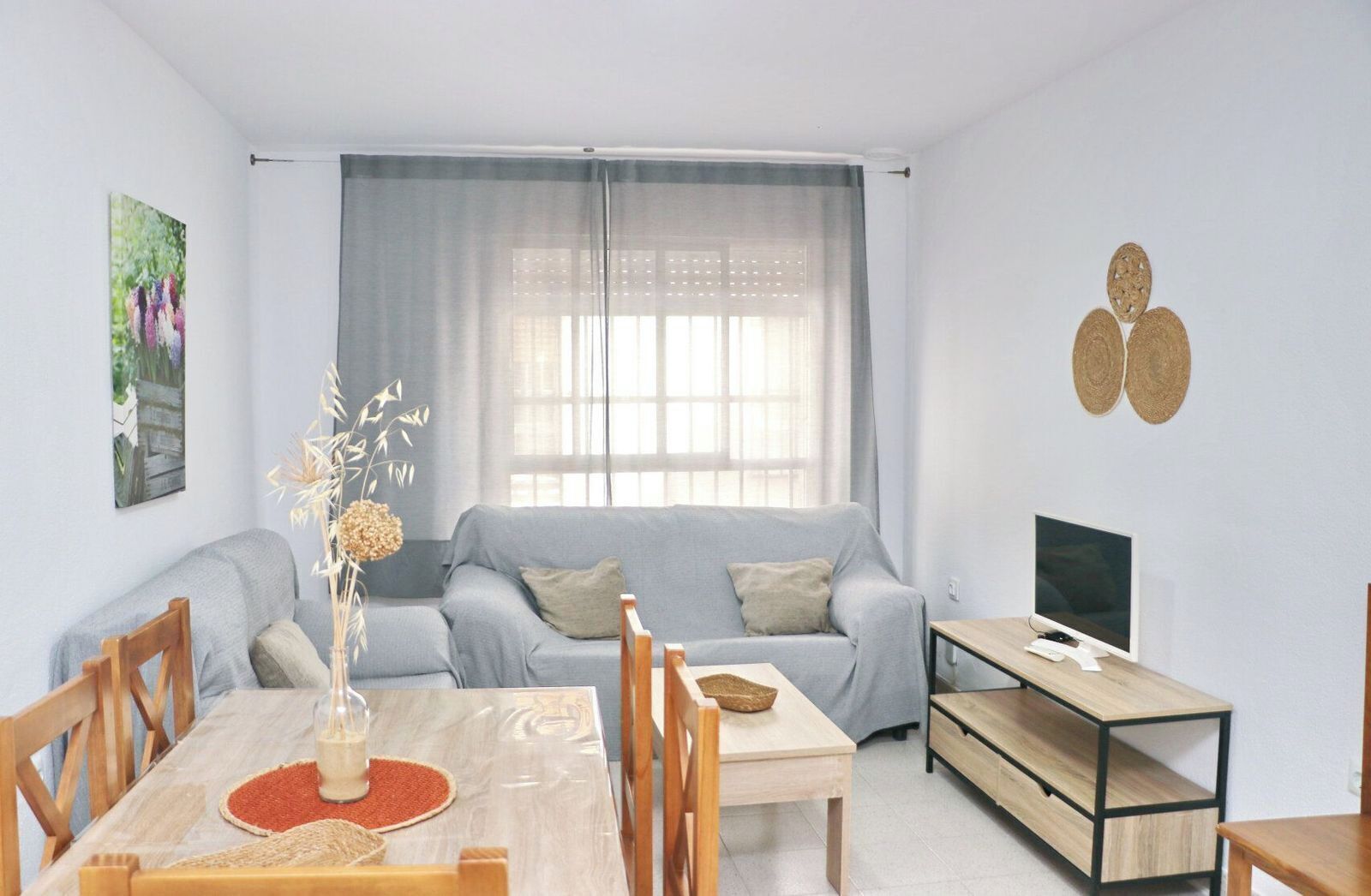 A modern living room with a grey sofa, a wooden dining table, and a TV on a wooden stand.