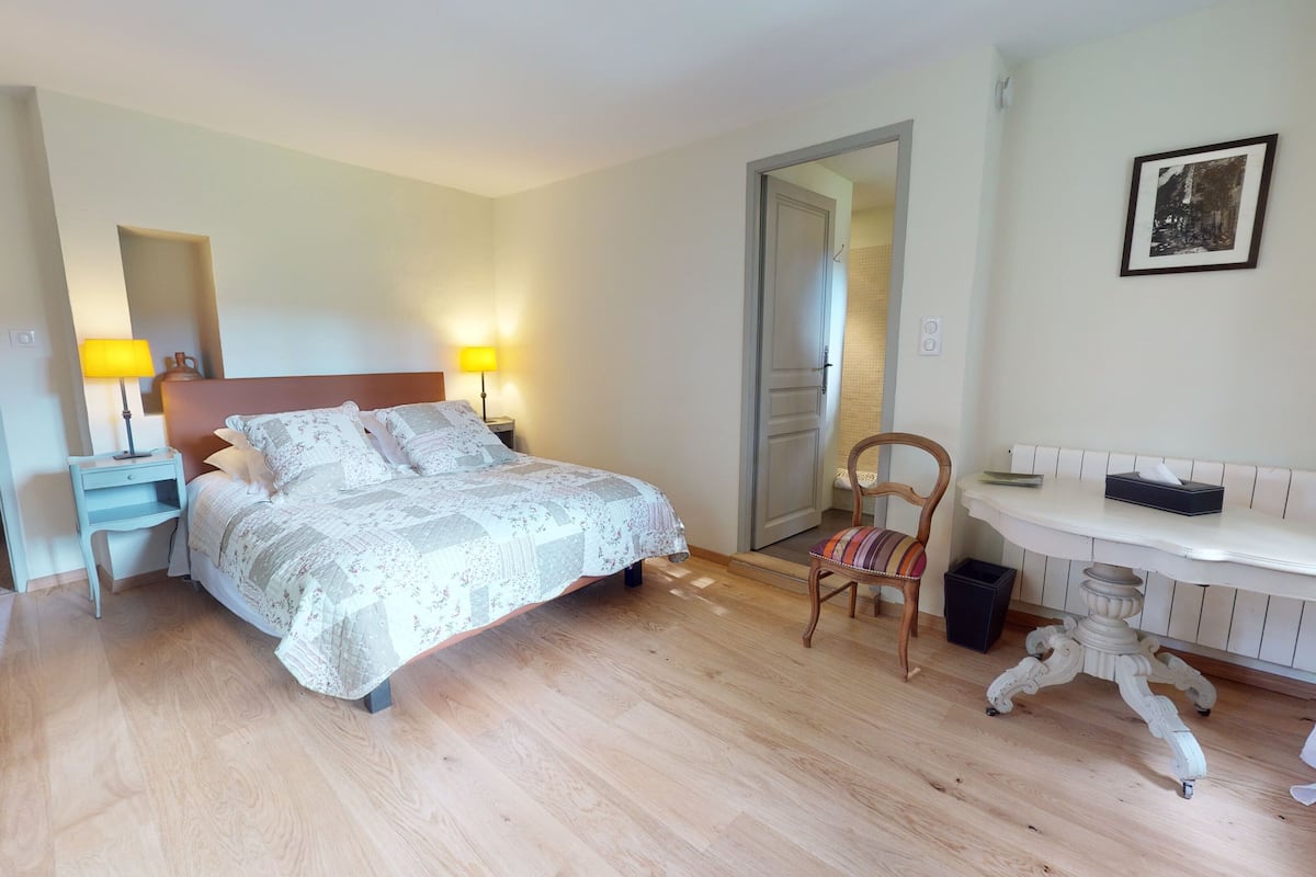 A bedroom with a bed, bedside lamps, a chair, a small table, and a mirror.