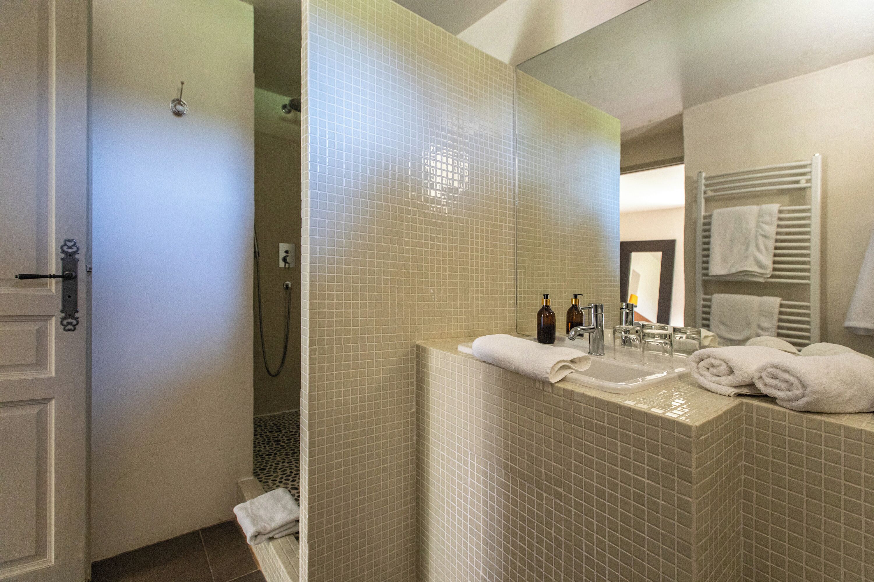 Een badkamer met een betegelde douche, een wastafel en een spiegel.