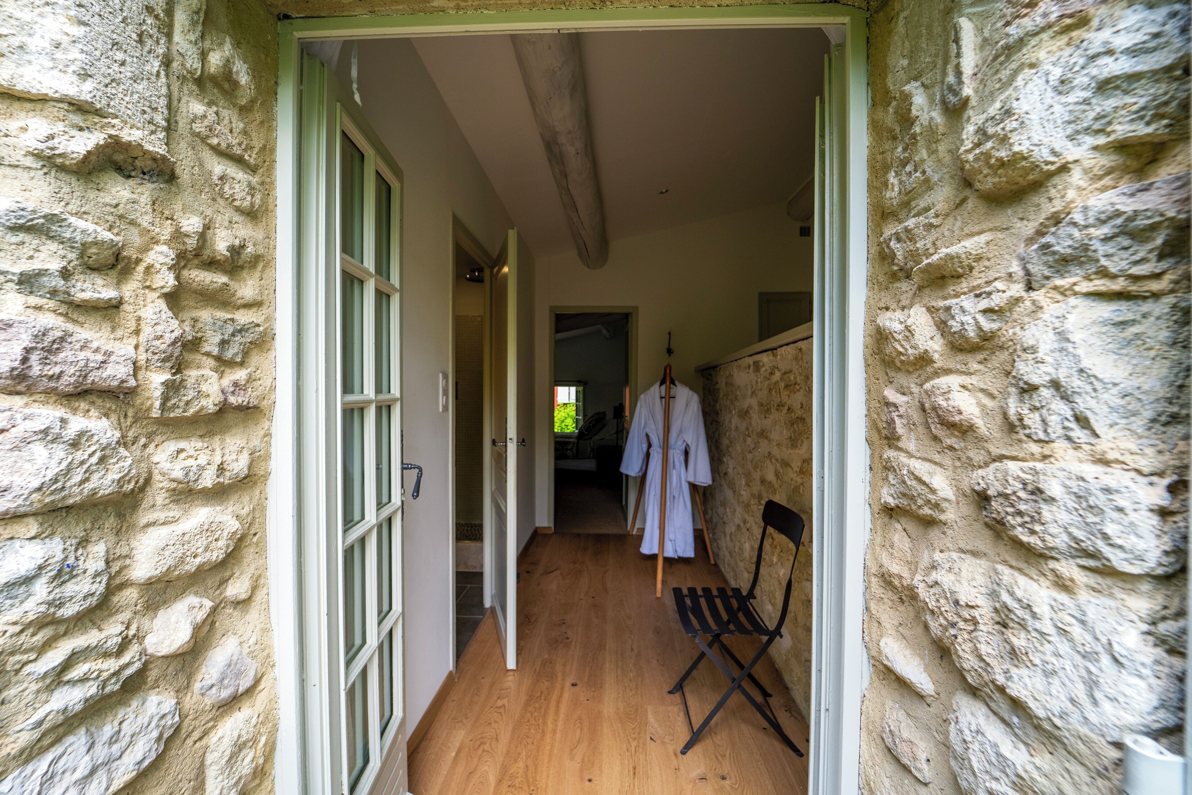 Un pasillo con paredes de piedra y suelo de madera, que conduce a una habitación con cama y ventana.