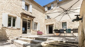 A stone building with a courtyard, outdoor seating, and a large umbrella. - Le Prieuré la Madelène (Malaucene)