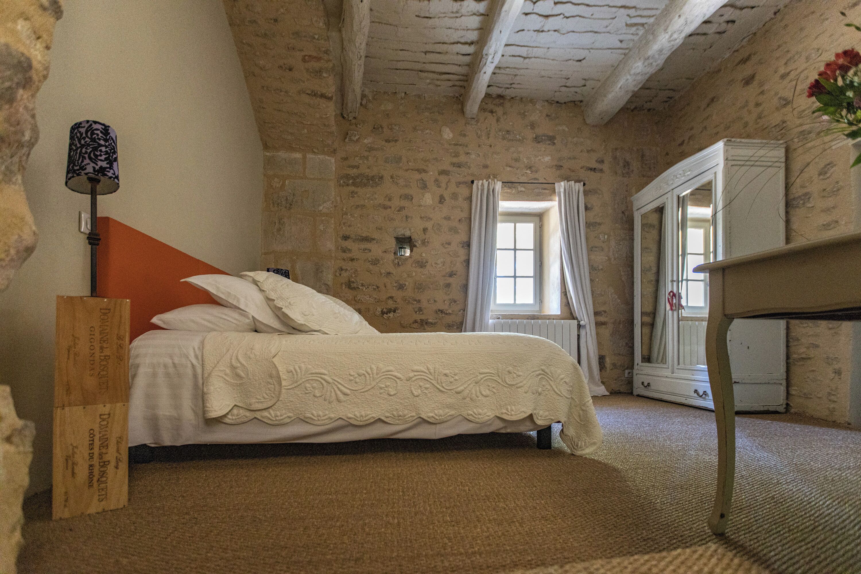 Ein Schlafzimmer mit einer Steinsandsteinwand, einem Bett mit weißen Leinen, einem hölzernen Nachttisch, einer Lampe und einem Spiegel.