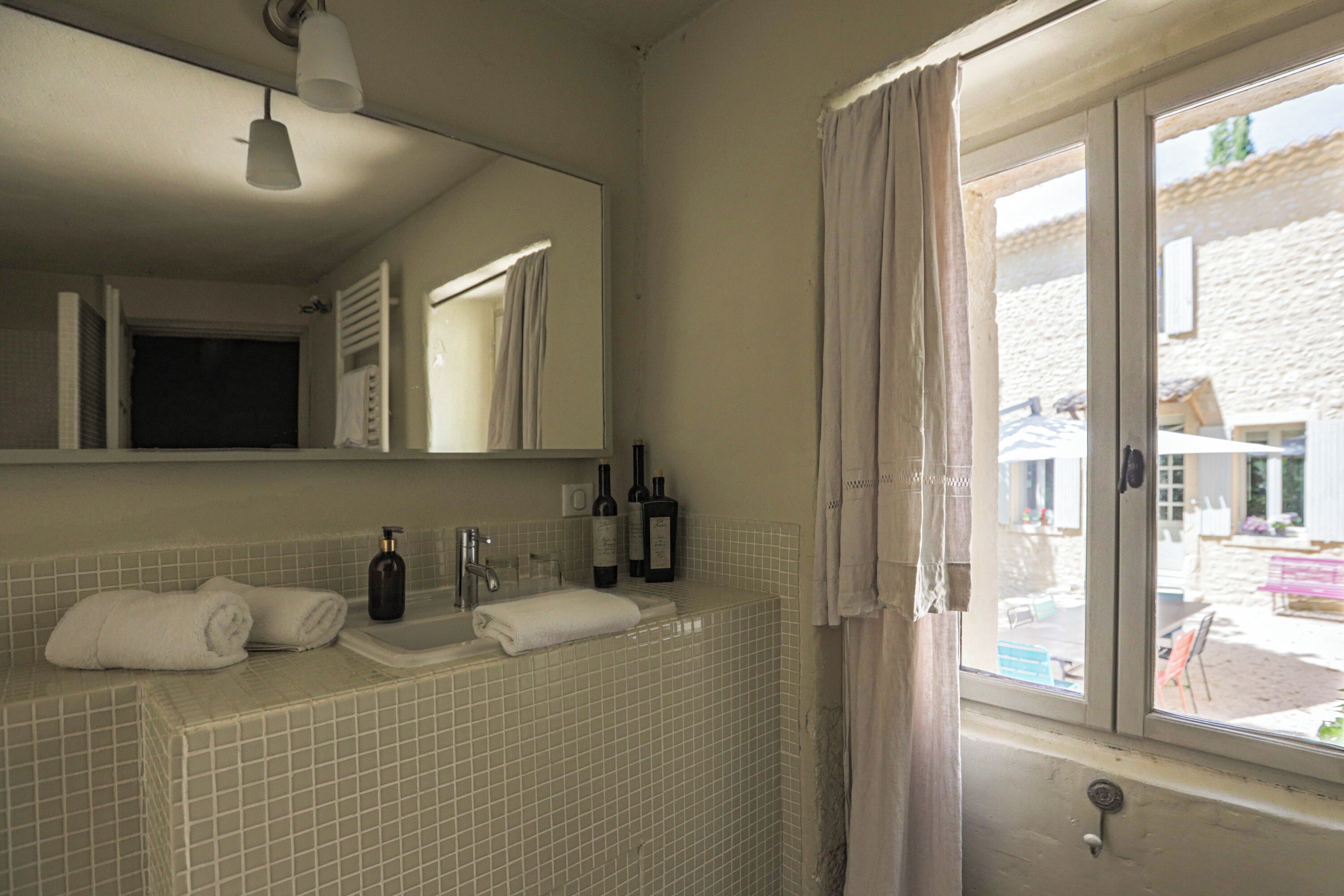 A bathroom with a tiled sink, two bottles of olive oil, and towels.