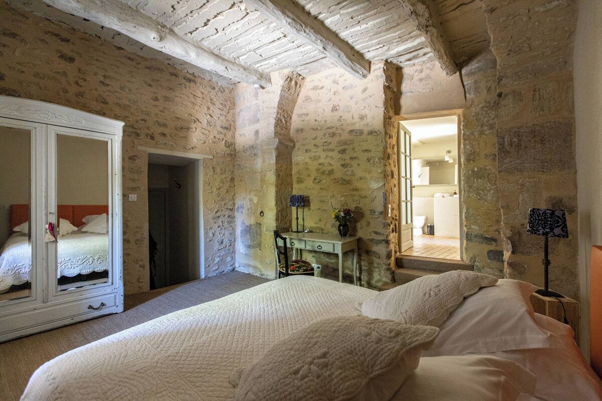 A bedroom with a large bed, a wardrobe, a desk, and a mirror.