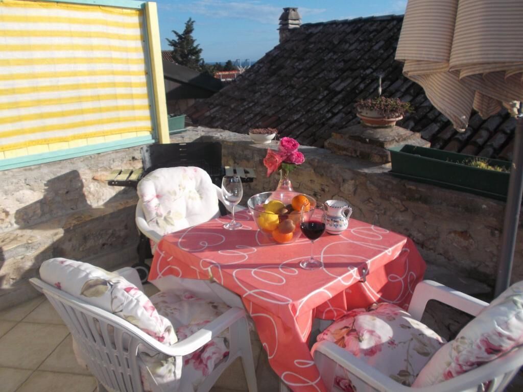 An outdoor dining area with a table set for two, covered with a pink tablecloth, and surrounded by white chairs with floral upholstery.