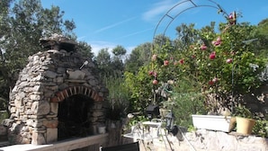 Un horno de piedra al aire libre con una rejilla de metal y una mesa con una botella y vasos.