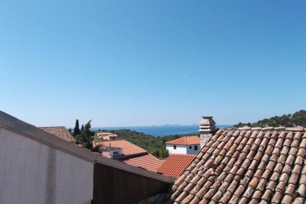 Vista de un pueblo costero con techos de tejas rojas, un cielo azul despejado y montañas a lo lejos.