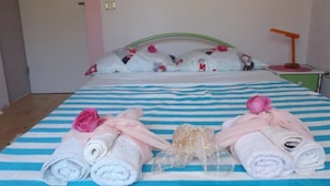 Una cama bien hecha con ropa de cama a rayas, almohadas con motivos florales y toallas enrolladas sobre una colcha azul y blanca a rayas.