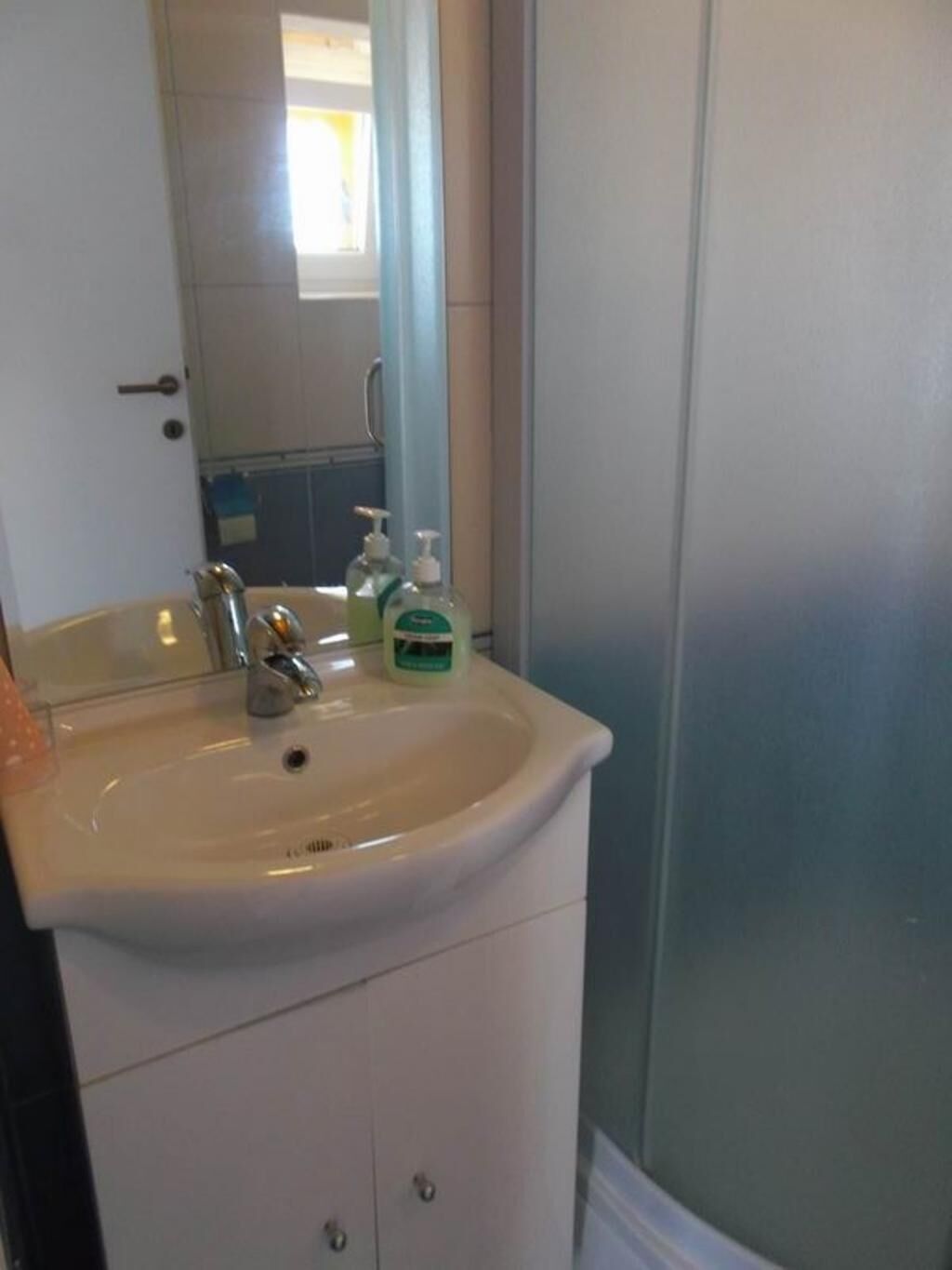 A bathroom with a white sink, a mirror, and a shower area.