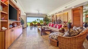A spacious living area with a large TV, comfortable seating, and a view of the outdoors. - Golf Villa 1102–Prime Location & Ocean Views | Onsite Staff & Daily Housekeeping (Kailua Kona)