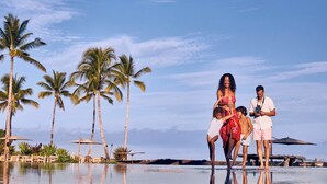 A poolside area with palm trees, a clear sky, and a person taking a photo. - Golf Villa 1102–Prime Location & Ocean Views | Onsite Staff & Daily Housekeeping (Kailua Kona)