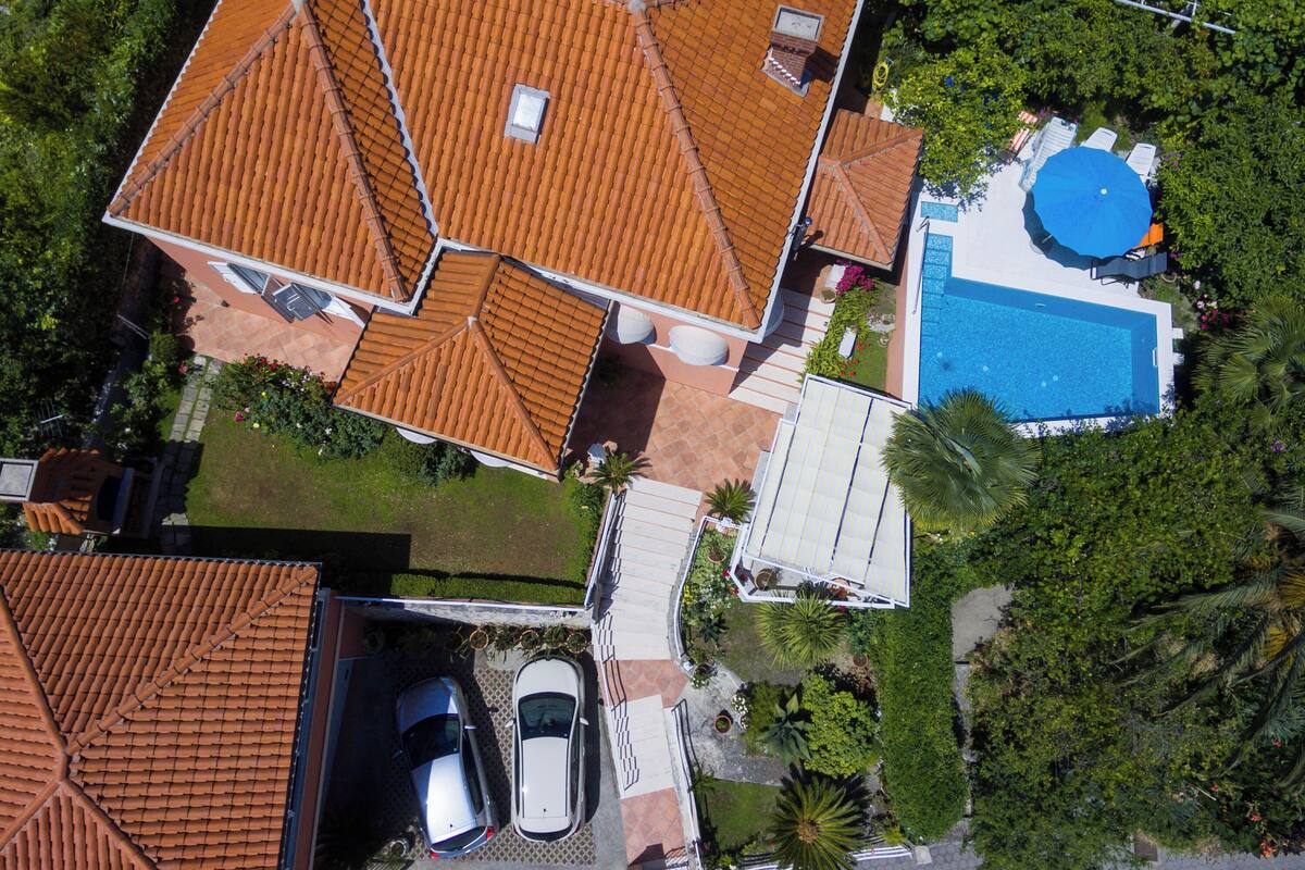 An aerial view of a residential property with a swimming pool, two cars, and a garden.