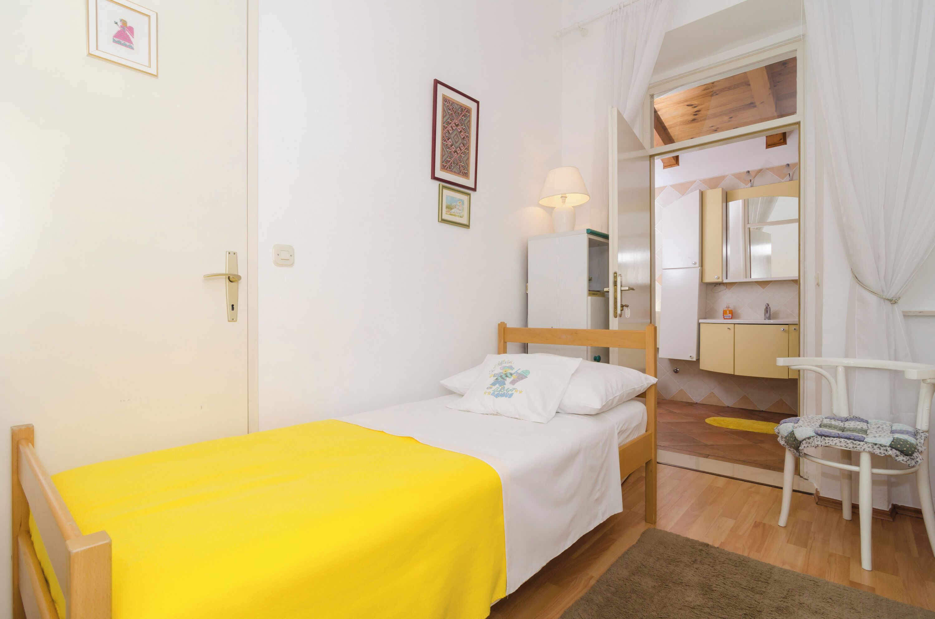 A small, bright room with a bed, a chair, a desk, and a mirror.