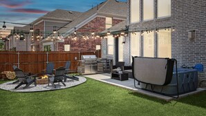Un patio trasero con zona de barbacoa, mobiliario exterior y un porche cubierto.