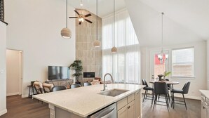 Una cocina amplia con una isla grande, modernos apliques colgantes y un comedor con mesa redonda y sillas.