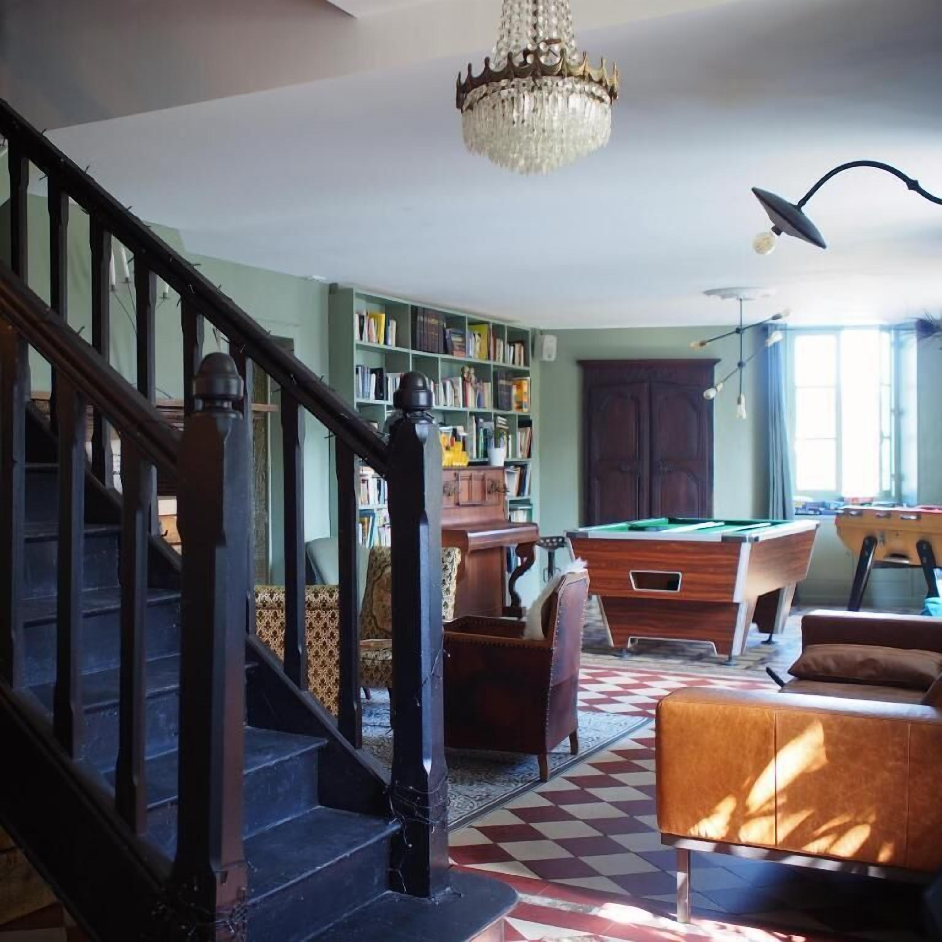 Een kamer met een wenteltrap, een pooltafel, een boekenkast en een kroonluchter.