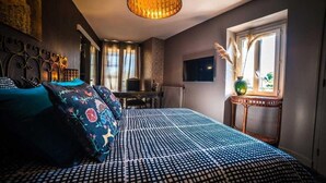 A bedroom with a patterned bedspread, a desk, a chair, a television, and a window with a vase of pampas grass. - Les chambres de Lily (Carresse-Cassaber)