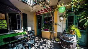 An outdoor seating area with a table and chairs, a wooden barrel planter, and a storefront with a sign reading "STELLA ARTES". - Les chambres de Lily (Carresse-Cassaber)