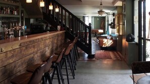 A bar area with wooden bar counter and stools, a staircase leading to a seating area with a patterned rug, and a view of the outside through a glass door. - Les chambres de Lily (Carresse-Cassaber)