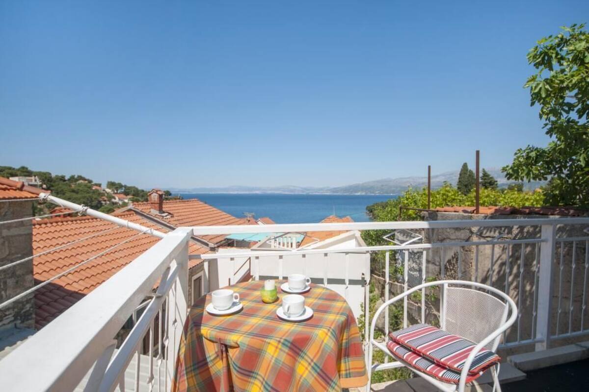A balcony with a table set for two, overlooking a coastal view.
