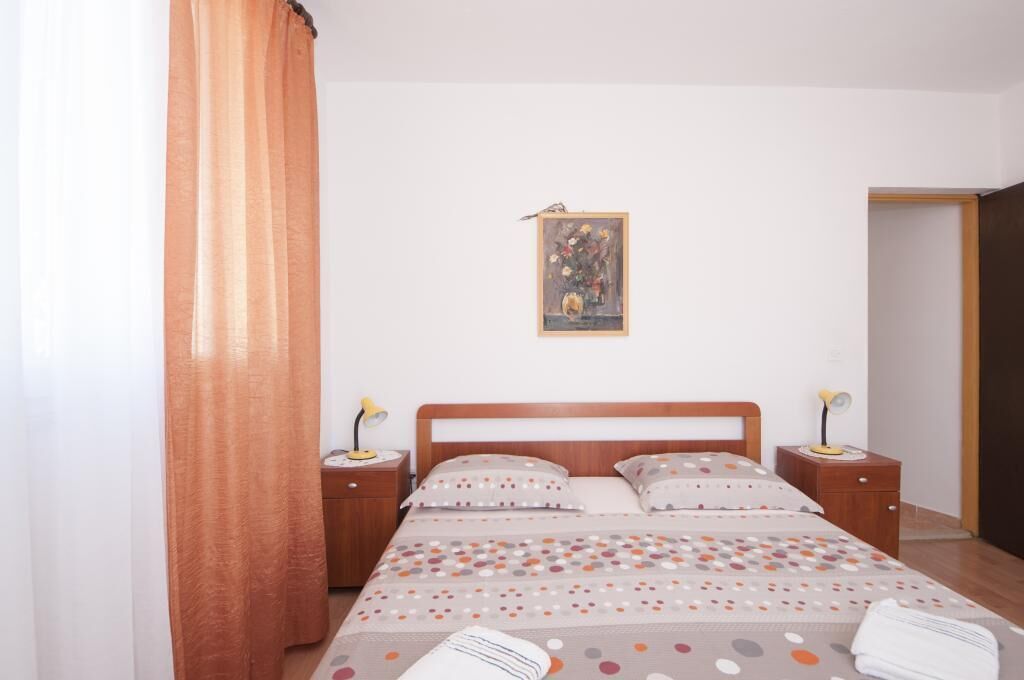 A bedroom with a bed, two bedside tables, a nightstand, a painting on the wall, and a door.