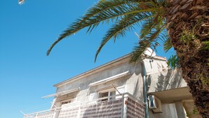 A building with a balcony, a palm tree, and a clear blue sky. - Apartments Mira (Supetar)