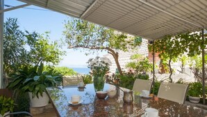 A covered outdoor dining area with a table set for two, surrounded by potted plants and a view of the sea. - Apartments Mira (Supetar)
