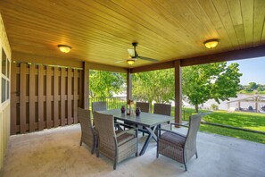 A covered patio with a table and chairs, a ceiling fan, and a view of a park and lake.
