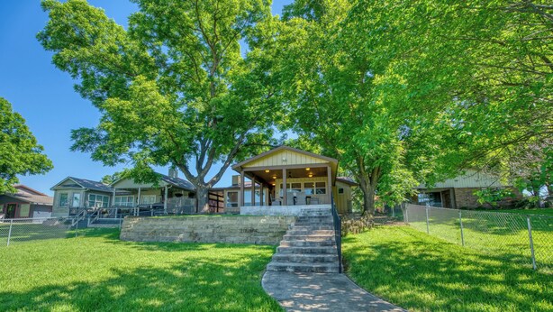 Una casa con porche, una escalera que lleva a la entrada y un patio cercado.