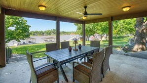 Un patio techado con mesa y sillas, un ventilador de techo y vistas a un parque y un lago.