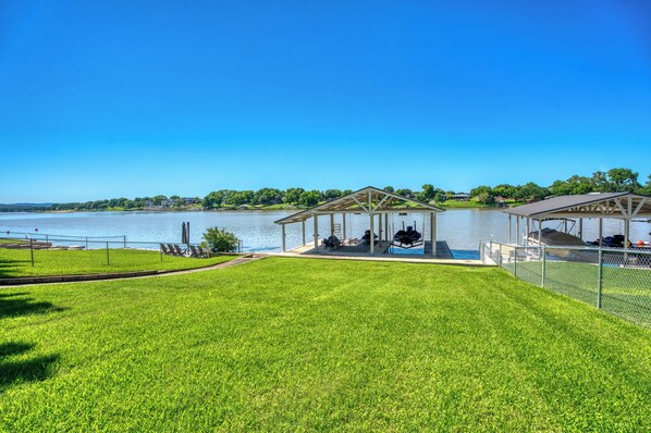 A lakeside property with a covered patio area, a swimming pool, and a well-maintained lawn.