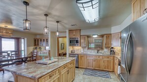 Una cocina amplia con armarios de madera, una isla grande, electrodomésticos de acero inoxidable e iluminación colgante.