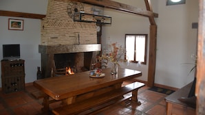 A rustic interior with a wooden table, a brick fireplace, and a television. - Maison de Campagne au Coeur de la Double Avec Piscine (Échourgnac)