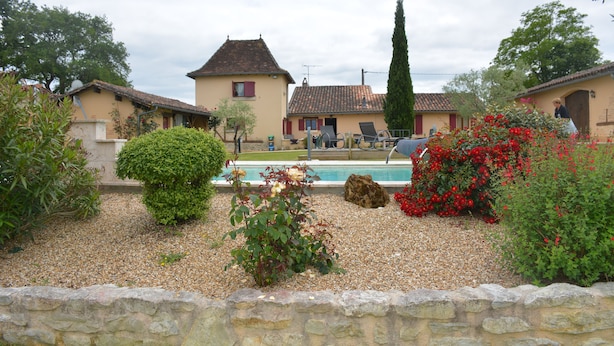 A residential area with a swimming pool surrounded by gravel, a stone wall, and various plants. - Maison de Campagne au Coeur de la Double Avec Piscine (Échourgnac)