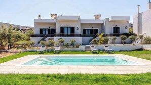 A modern two-story building with a swimming pool, outdoor seating, and a well-maintained garden.