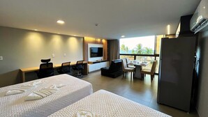Habitación de hotel con dos camas, televisión, zona de comedor y vistas al exterior.