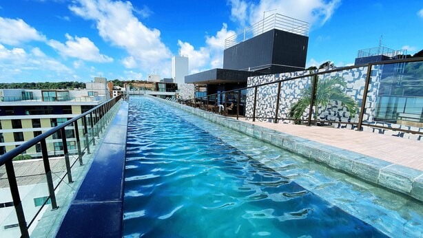 Una larga piscina con una barrera de cristal en un lado y un muro decorado en el otro.
