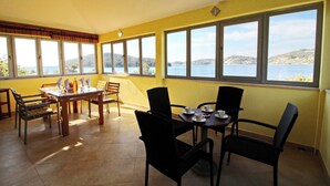 A dining area with a table set for four, large windows with a view of the sea, and yellow walls.