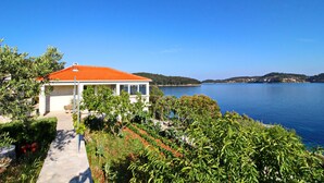 A coastal house with a red roof, surrounded by lush greenery and a view of the sea.