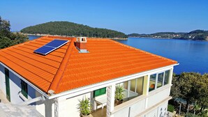 A modern house with a red tiled roof, a solar panel, and a view of a lake and hills.